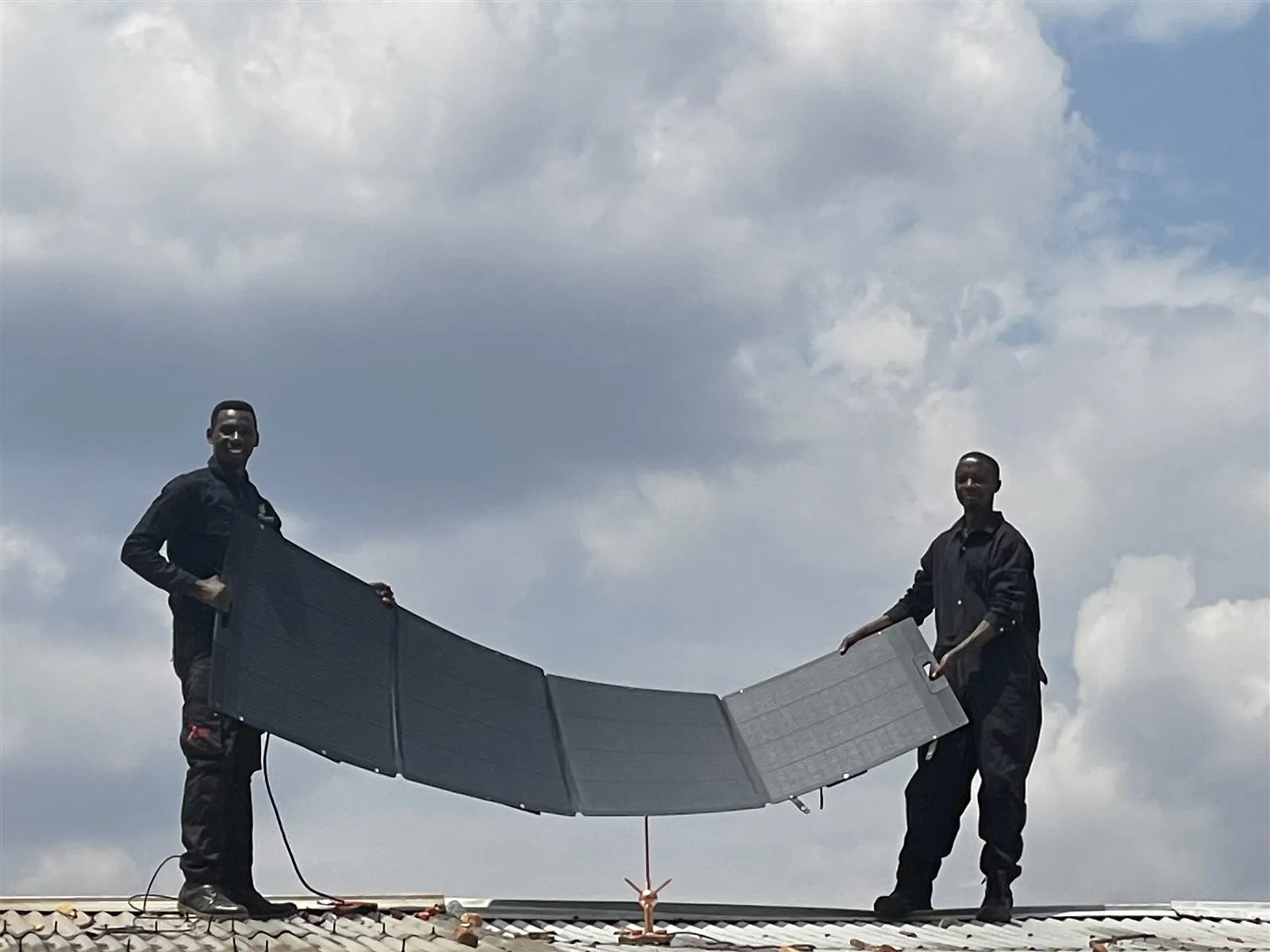 Deux techniciens STS tiennent un panneau solaire sur le toit de l’école